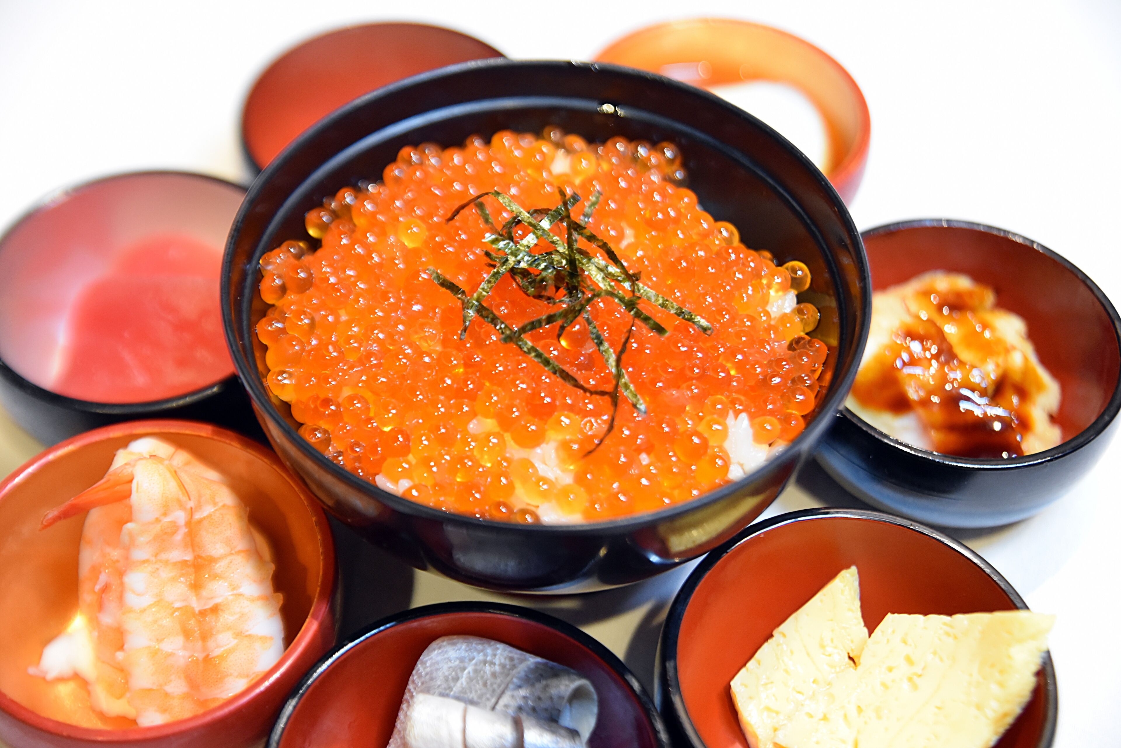 A bowl of salmon roe with a garnish, surrounded by various small dishes.