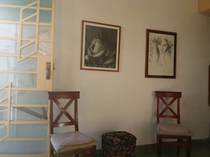 Ein Zimmer mit zwei Holzsesseln, einer mit Kissen und der andere mit Blumenmuster. An der Wand hängen zwei gerahmte Kunstwerke.