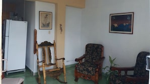 Olohuoneessa on puinen keinutuoli, kukkakuviollinen nojatuoli ja seinällä taulu.