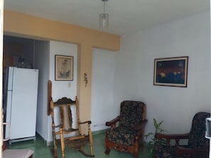 Ein Wohnzimmer mit einem Holzschaukelstuhl, einem blumigen Sessel und einem Gemälde an der Wand.