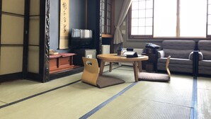 Una habitación japonesa tradicional con suelo de tatami, una mesa baja con cojín, un sofá y un televisor.