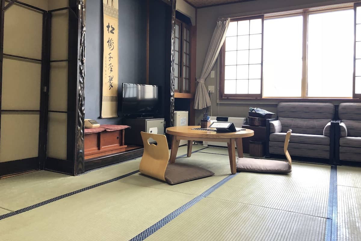Ein traditioneller japanischer Raum mit Tatami-Böden, einem niedrigen Tisch mit Kissen, einer Couch und einem Fernseher.