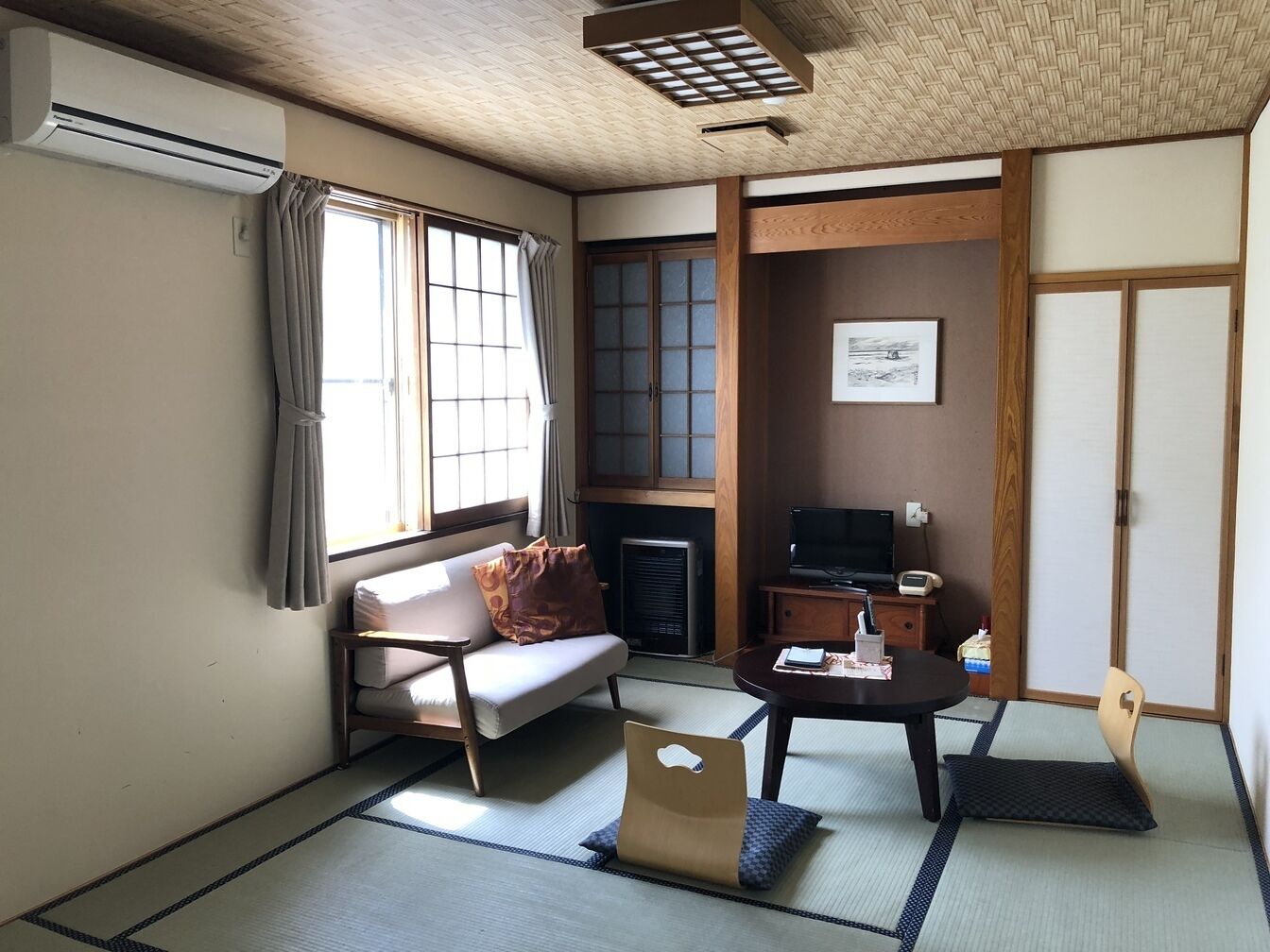 A traditional Japanese room with tatami flooring, a futon bed, a television, and a fireplace.