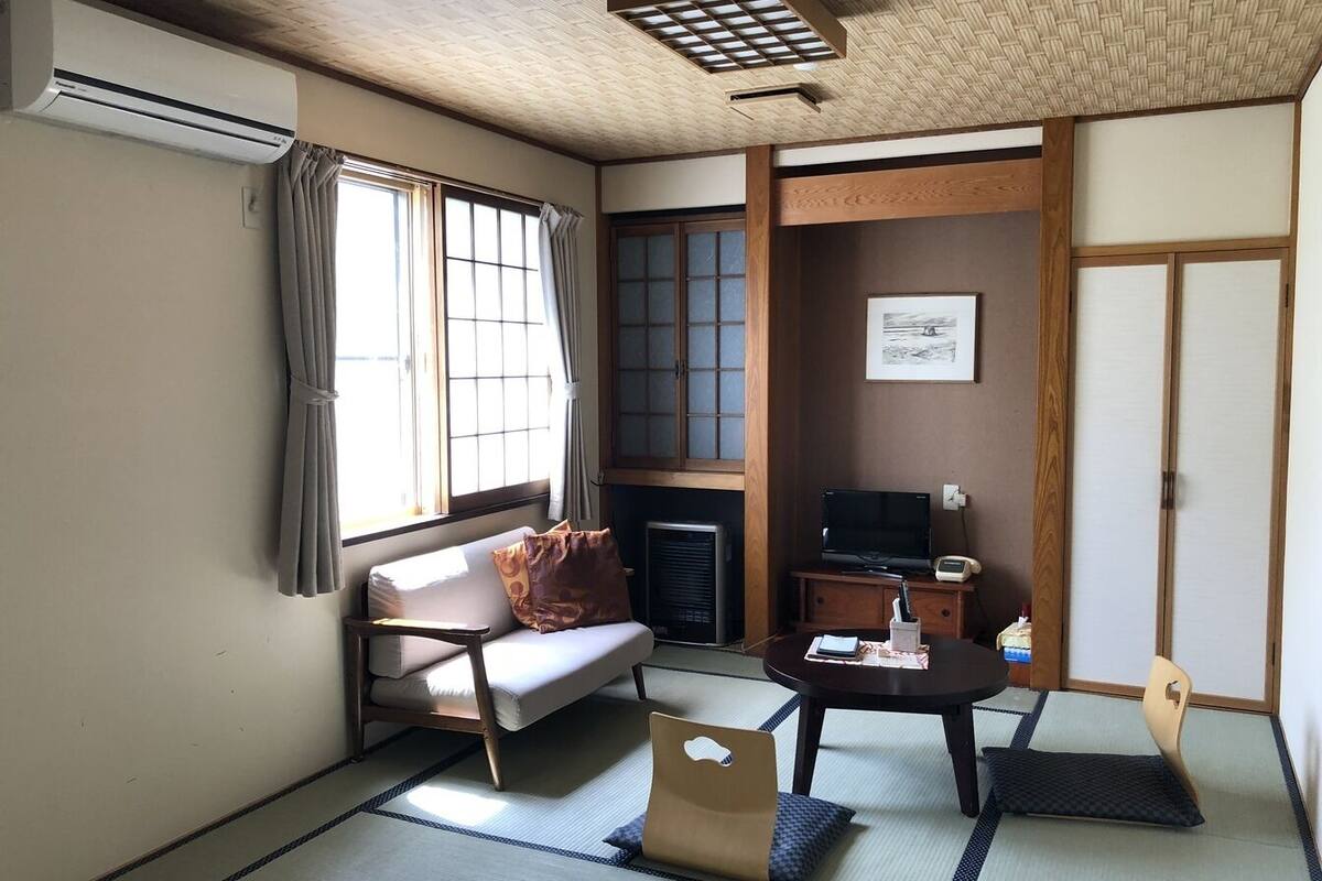 Ein traditioneller japanischer Raum mit Tatami-Böden, einem Futonbett, einem Fernseher und einem Kamin.
