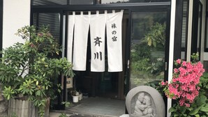 Una entrada tradicional japonesa con una estatua de piedra, plantas en macetas y un cartel que dice '旅の宿'.