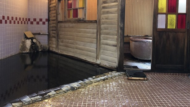 Un onsen japonés tradicional con interior de madera, una cuenca de piedra y suelo de baldosas.