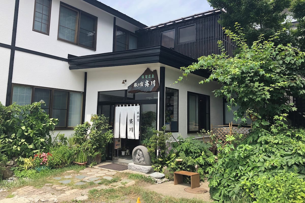 Ein traditionelles japanisches Gebäude mit überdachter Eingangspartei, Kiesweg und üppigem Grün.