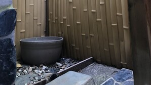 Un pequeño espacio al aire libre con cerca de bambú, una maceta grande con plantas jóvenes y un camino de piedra.