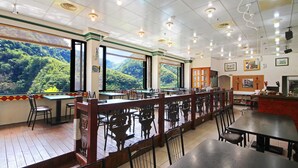Un restaurant doté d’un plancher, de tables et de chaises en bois. De grandes fenêtres offrent une vue sur une zone boisée.