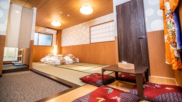 A traditional Japanese room with tatami flooring, a low bed, a wooden table, and a sliding door. - Kujira Vip (Osaka)