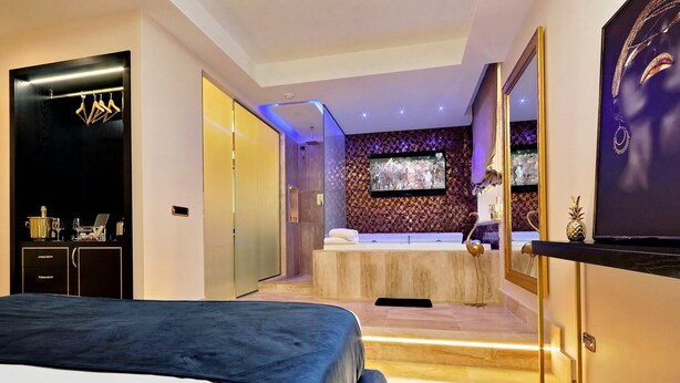 A modern hotel room with a large bed, a bathroom with a bathtub, and a TV mounted on the wall. - Spanish Diamond Luxury Suites & Jacuzzi (Rome)