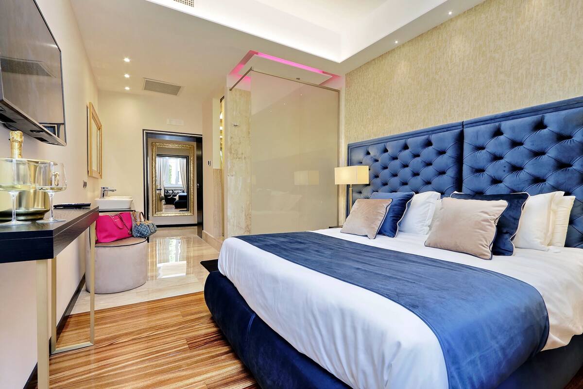 A modern hotel room with a large bed, a vanity with a mirror, and a small seating area.