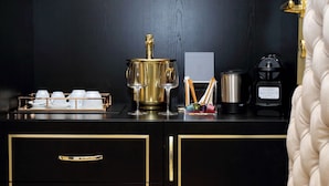 A black and gold minibar with a coffee maker, a wine glass, and a tray of white cups. - Spanish Diamond Luxury Suites & Jacuzzi (Rome)