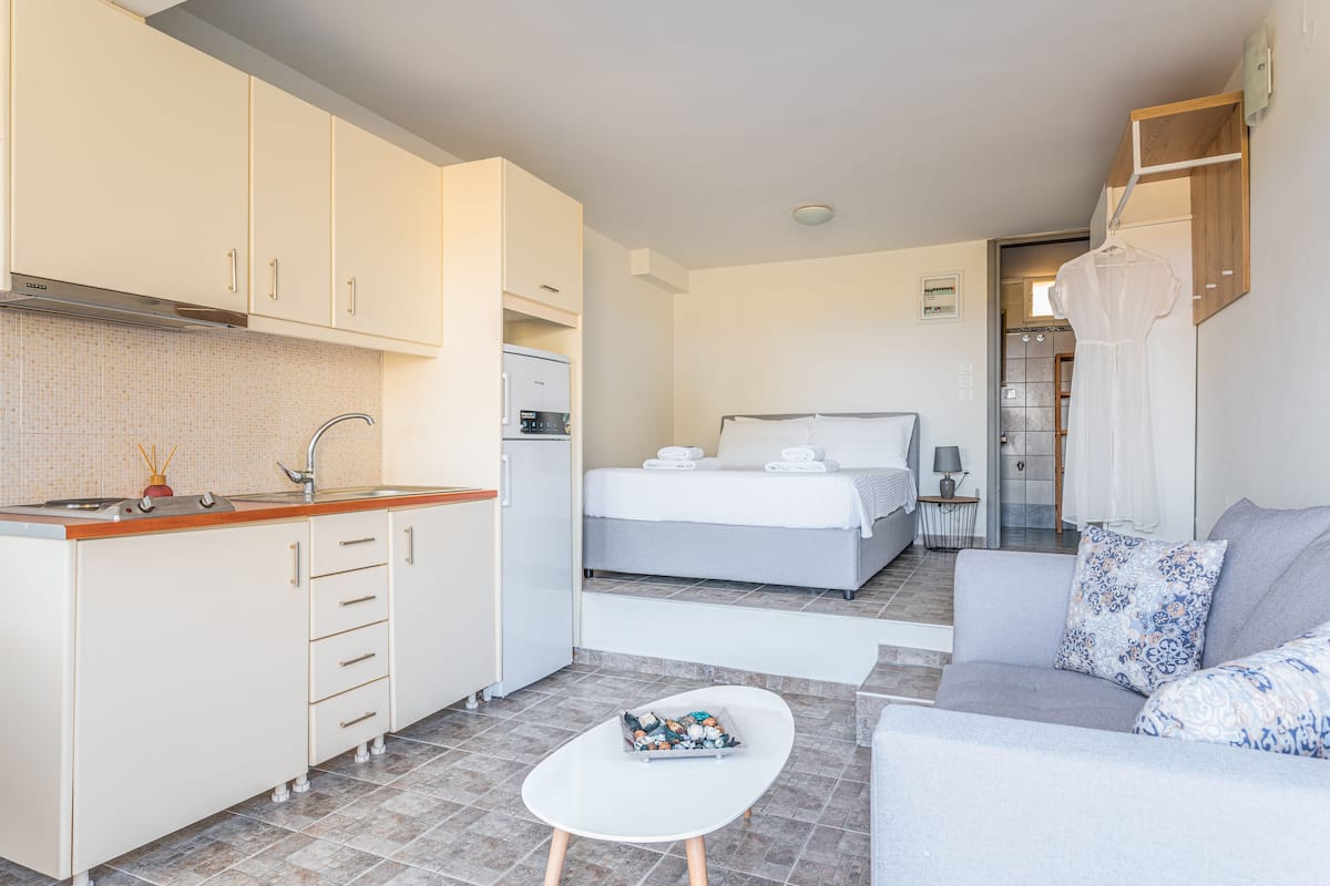 A compact hotel room with a kitchenette, a bed, a sofa, and a small table.