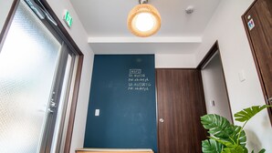 L’entrée d’un hôtel, avec une porte bleu foncé, un banc en bois, un pot de fleurs et un mur à la texture particulière.
