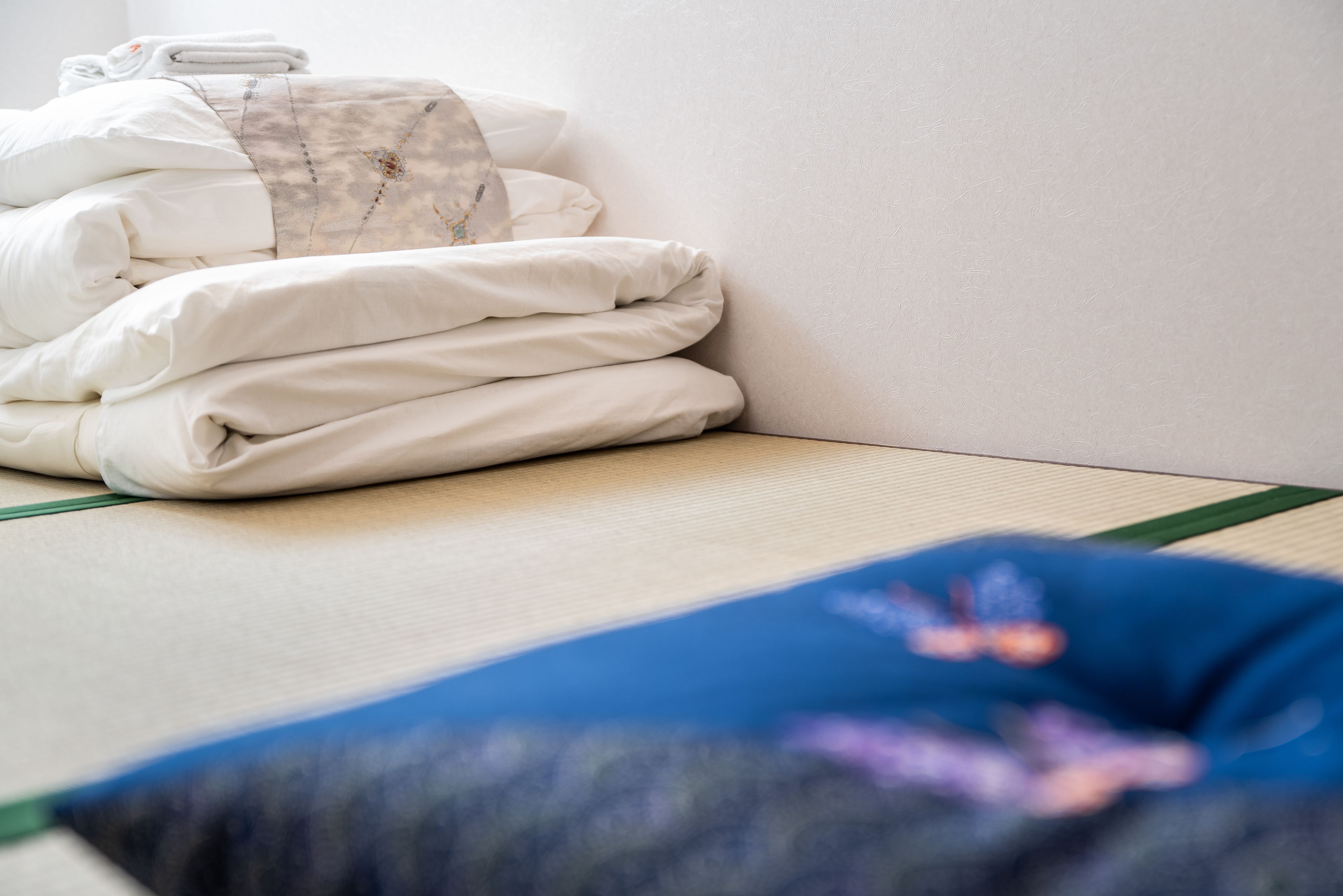 A neatly made bed with white bedding and a blue pillow with a floral pattern.