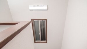 Un escalier étroit, doté de rampes en bois et de marches recouvertes de moquette, mène à une pièce avec une fenêtre et un appareil de climatisation fixé au mur.