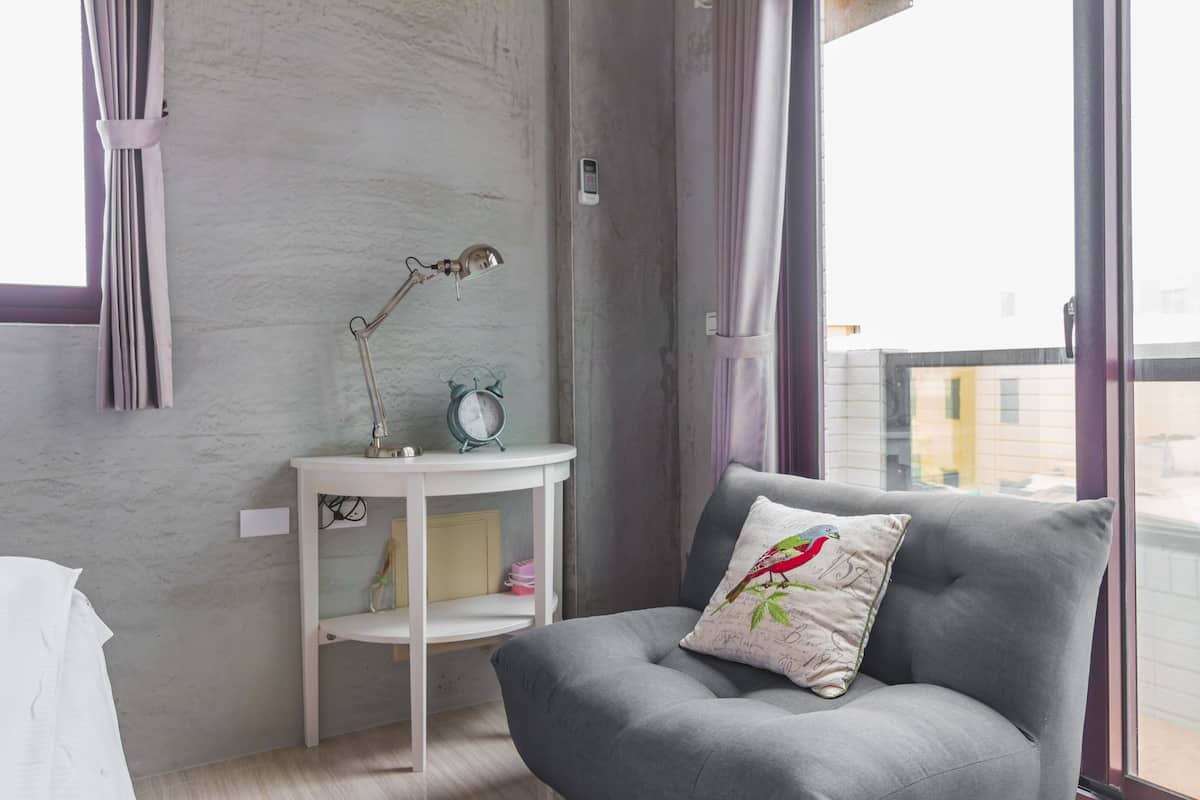 A modern room with a grey sofa, a small white side table with a lamp, and a window with curtains.