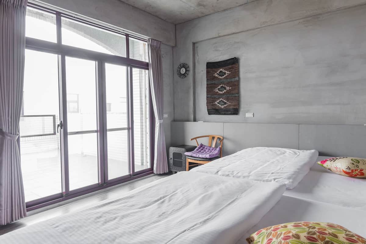 A bedroom with a large window, a bed, a chair, and a wall-mounted clock.