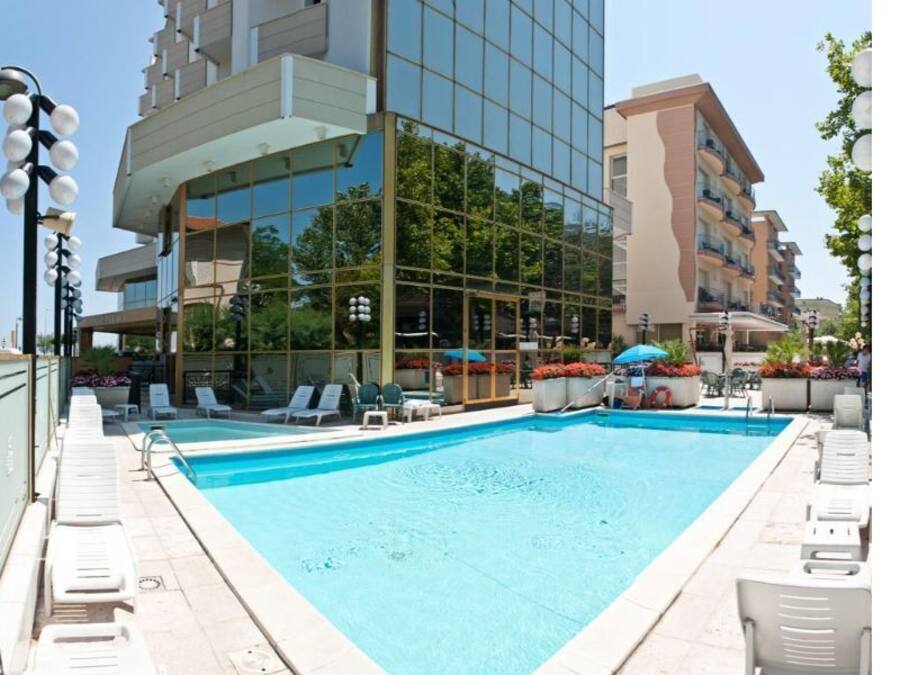 A swimming pool with lounge chairs and umbrellas, surrounded by modern buildings.