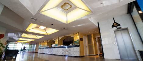 A spacious lobby with a marble reception desk, geometric ceiling lights, and a modern design.