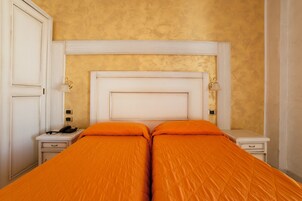 Un letto matrimoniale con una coperta arancione, una testiera bianca e comodini con lampade.