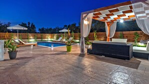 An outdoor patio area with a pool, seating, and a pergola with draped fabric. - Villa Eleon with private pool, BBQ and beautiful garden. (Zakynthos)