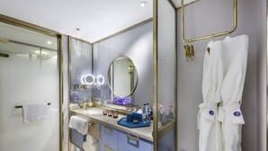 Un baño moderno con cabina de ducha de vidrio, tocador con espejo e iluminación, y una bata colgada en un perchero.