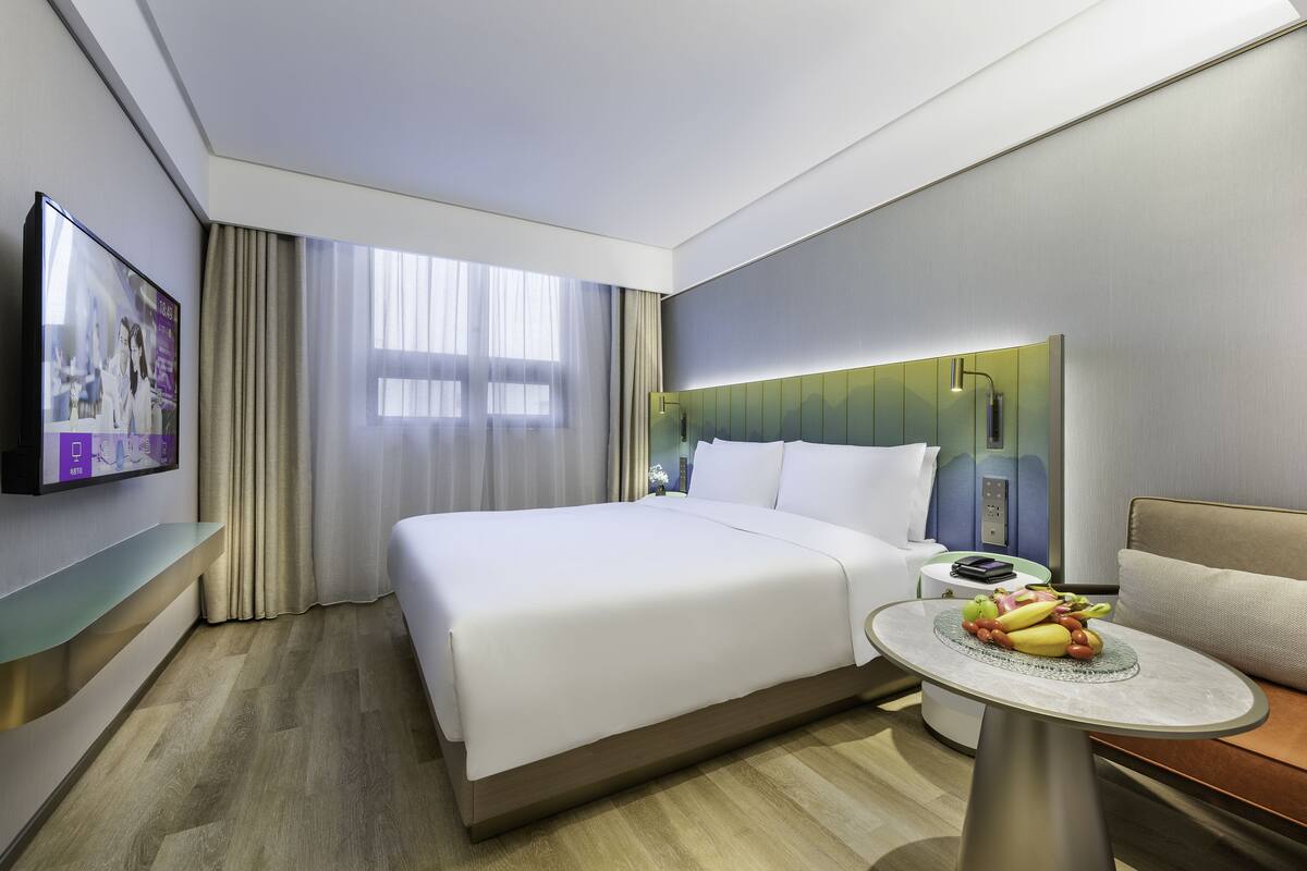 Een moderne hotelkamer met een groot bed, een nachtkastje met fruit, een televisie en uitzicht op de stad.