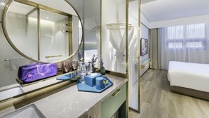 Habitación de hotel con un espejo grande, una cama, una tocador con artículos de aseo y vistas de la ciudad desde la ventana.