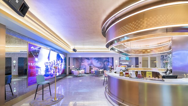 Un moderno vestíbulo de hotel con un mostrador de recepción, zona de estar y una gran pantalla digital que muestra un evento.