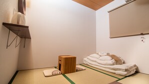 A traditional Japanese room with tatami flooring, a wooden stool, a futon bed, and a small shelf with a mirror and a light fixture. - Kujira 202 (Osaka)