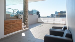 Eine moderne Dachterrasse mit einer Holzbank, einem Glasgeländer und Blick auf die Stadtlandschaft.