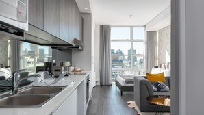 Eine moderne Küche mit Einbauherd, einem großen Fenster mit Blick auf die Stadt und einem grauen Sofa mit gelbem Kissen.
