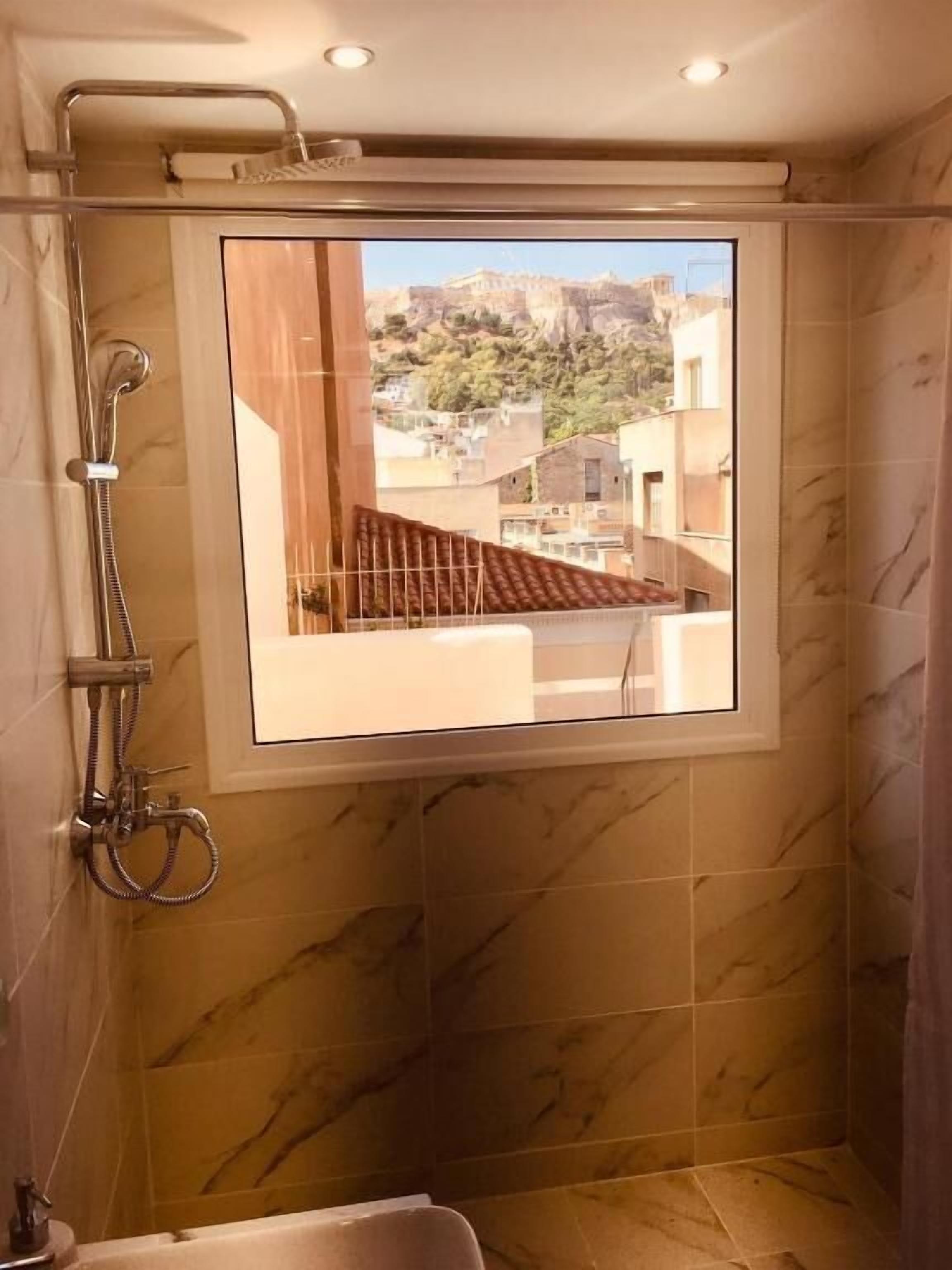 A shower with a view of a residential area, marble tiles, and a showerhead.