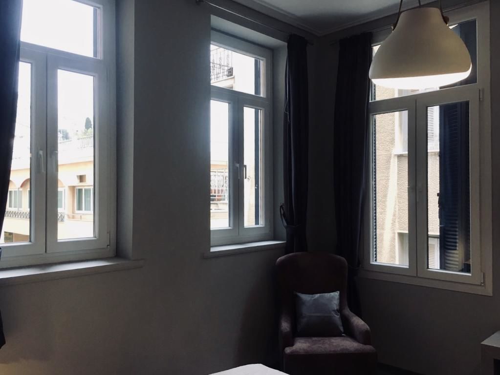 Une pièce avec deux fenêtres, une chaise et un luminaire suspendu.