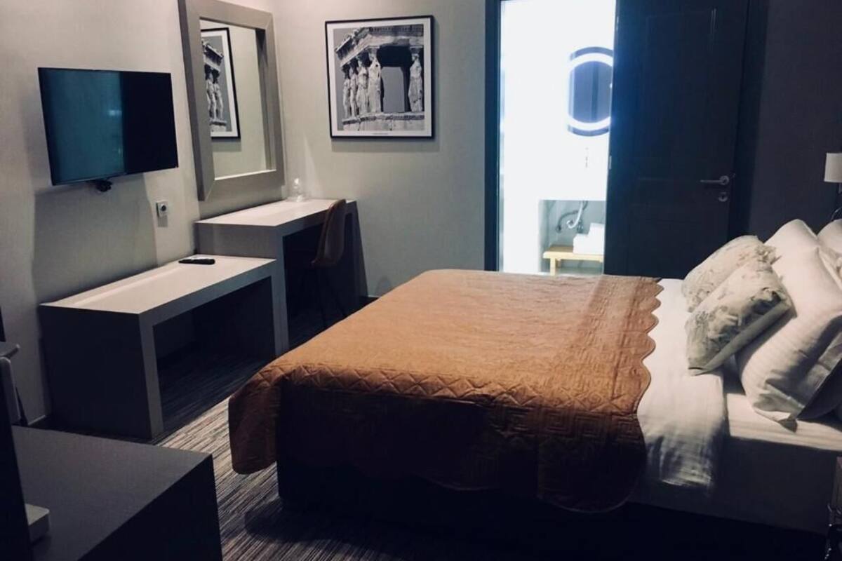 A hotel room with a bed, a desk, a TV, and a door leading to a balcony.