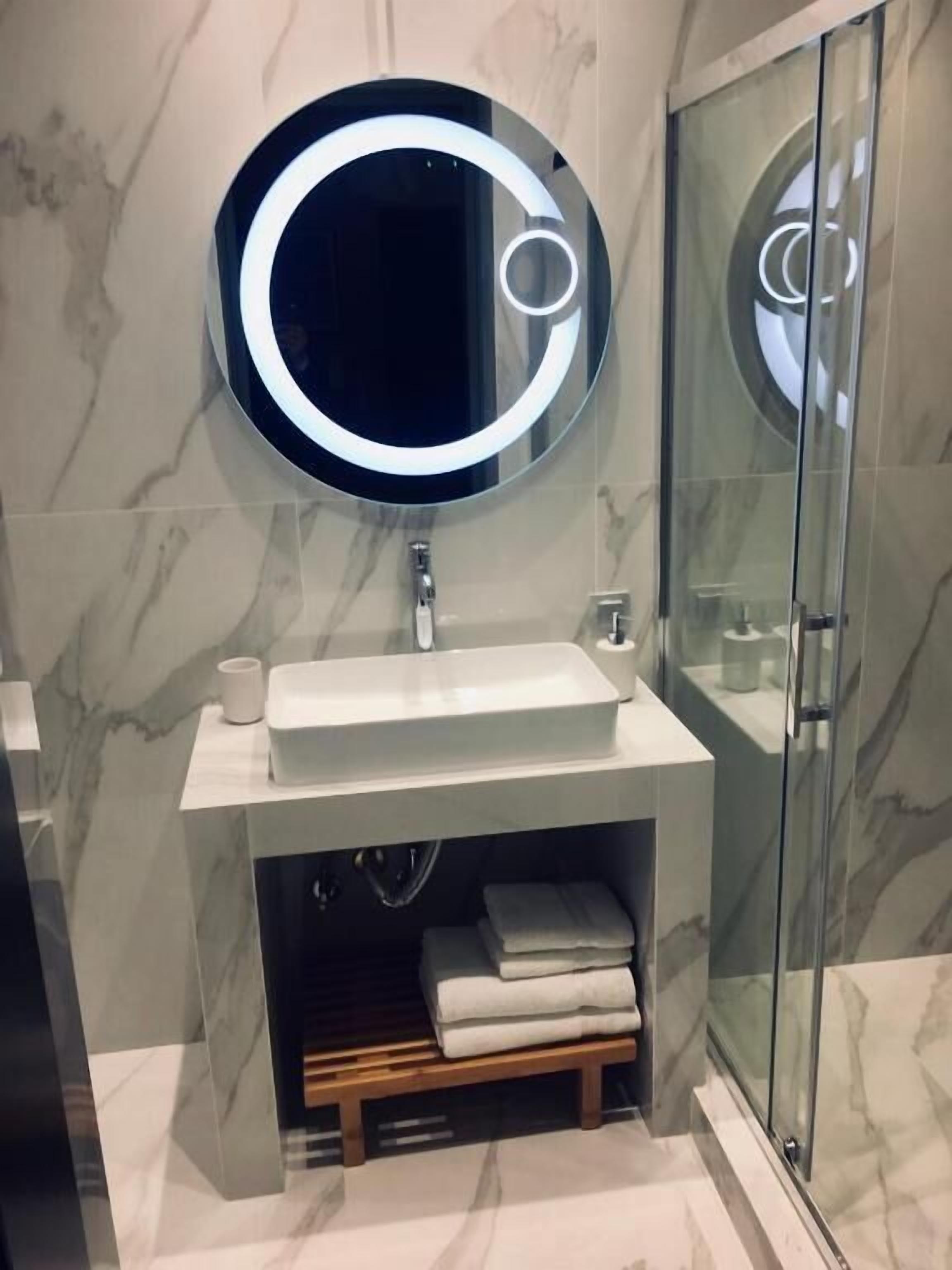 A modern bathroom with a round mirror, white sink, and glass shower enclosure.