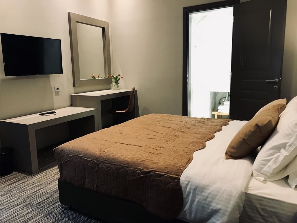 A hotel room with a bed, a desk with a chair, a TV mounted on the wall, and a door leading to a balcony.