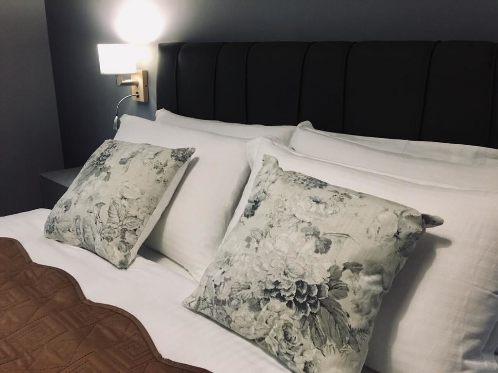 A bed with floral-patterned pillows, a headboard, and a bedside lamp.