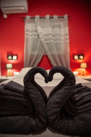 Habitación de hotel con una pared roja, una cama con ropa blanca y una disposición de toallas con forma de corazón sobre la cama.