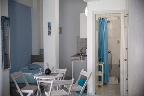 Habitación de hotel compacta con cama, una pequeña mesa con sillas, kitchenette y zona de ducha.