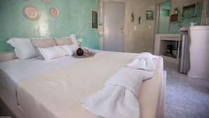 A bedroom with a bed, a bedside table, a mirror, and a bathroom with a sink and mirror. - Pasithei Studios (Santorini)