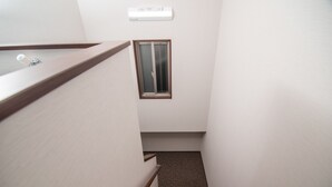 A narrow stairway with a wooden handrail, a small window with a metal screen, and a wall-mounted air conditioning unit. - Kujira 203 (Osaka)