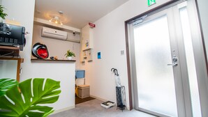 A hotel room with a door, a scale, a plant, a shelf with a helmet, and an air conditioning unit. - Kujira 203 (Osaka)