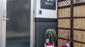 A hotel entrance with a sliding glass door, a sign with a bird logo, and a bamboo fence. - Kujira 203 (Osaka)