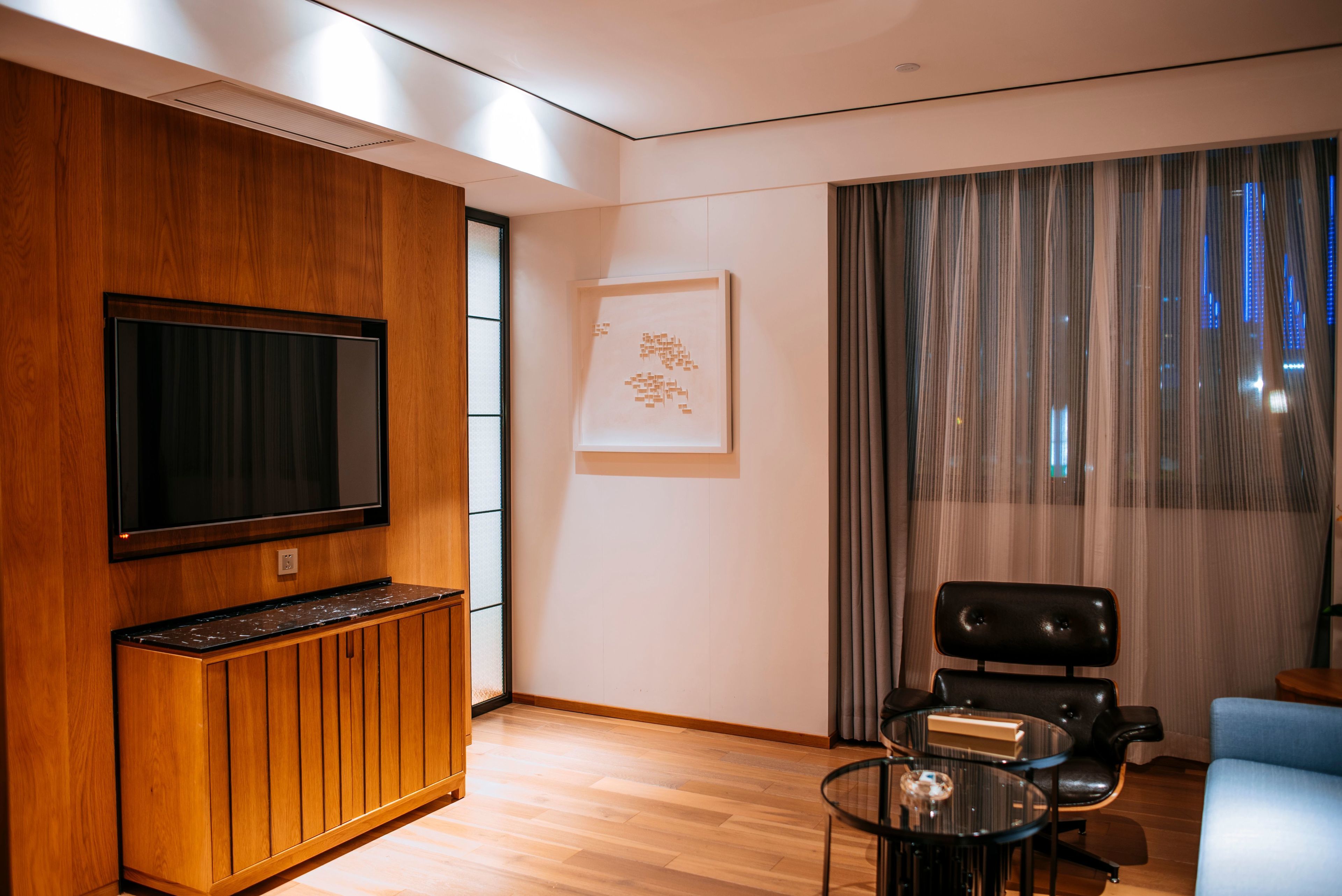 A modern living room with a flat-screen TV, wooden cabinet, and a glass coffee table.