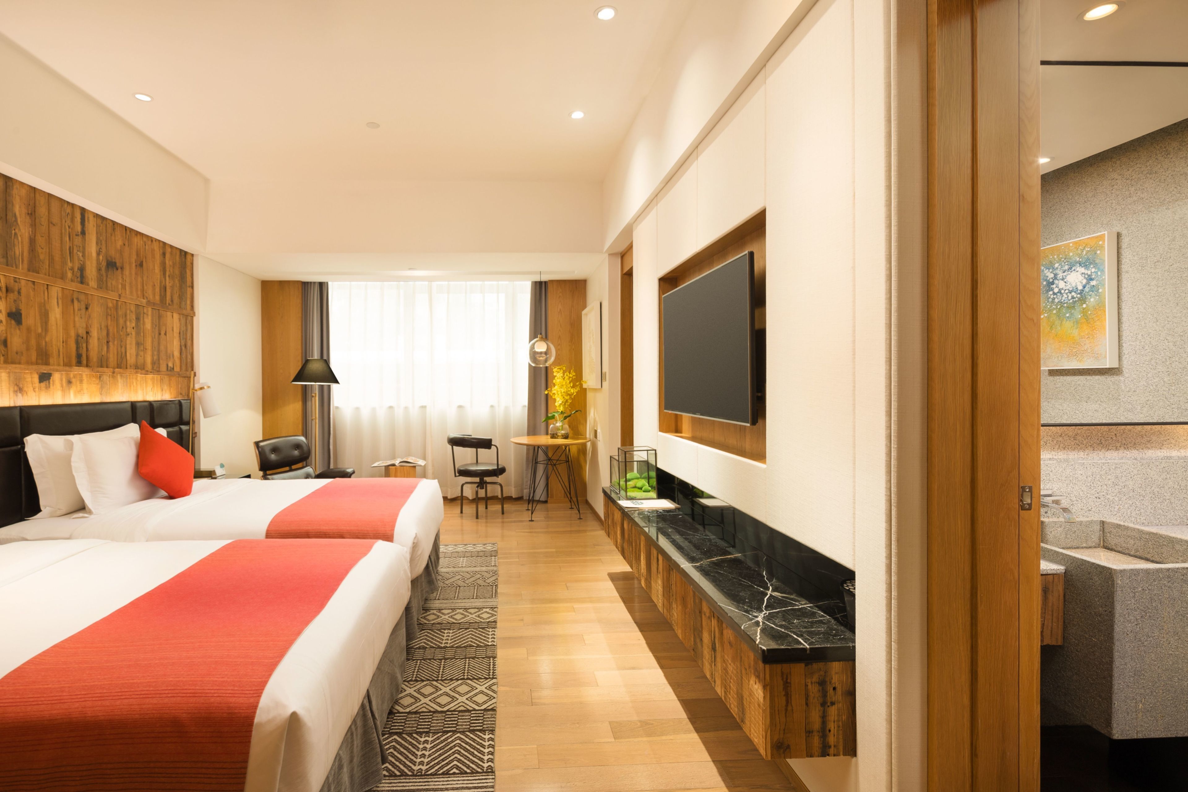 A hotel room with two beds, a TV, a desk, and a bathroom.