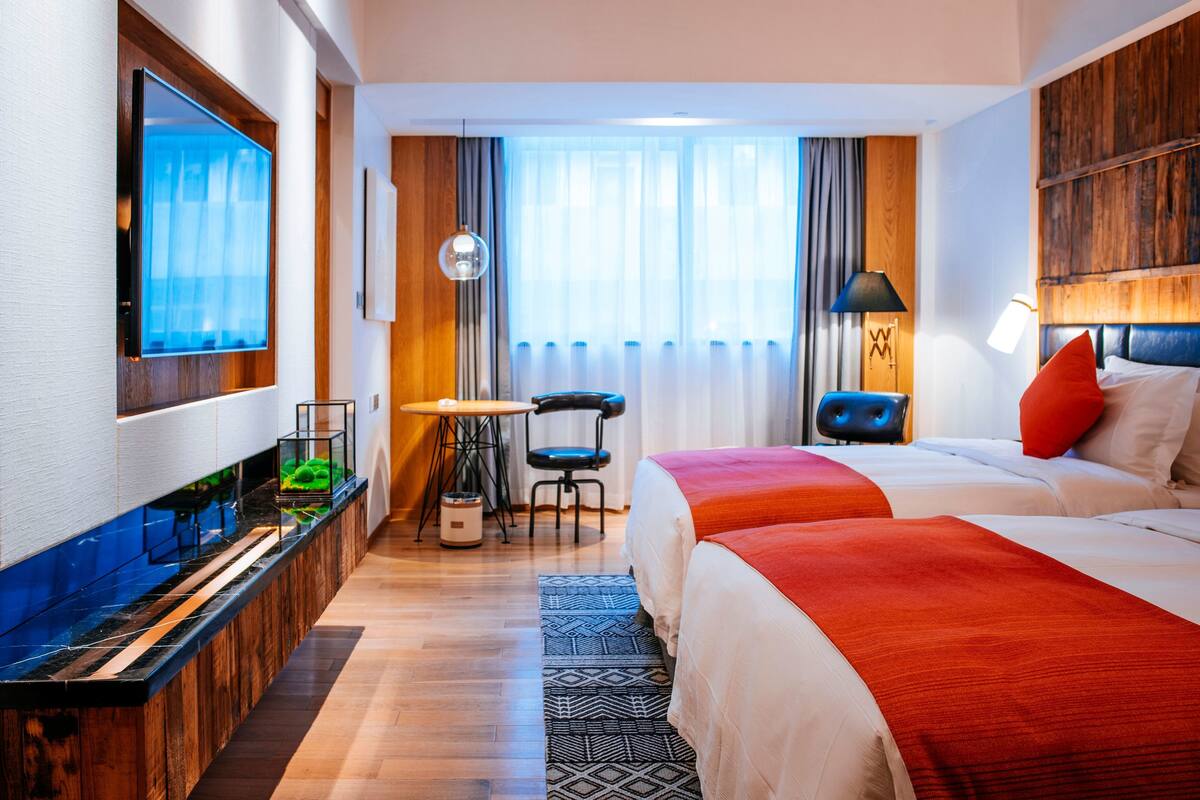 A hotel room with a large bed, a desk, a chair, a TV, and a window with curtains.