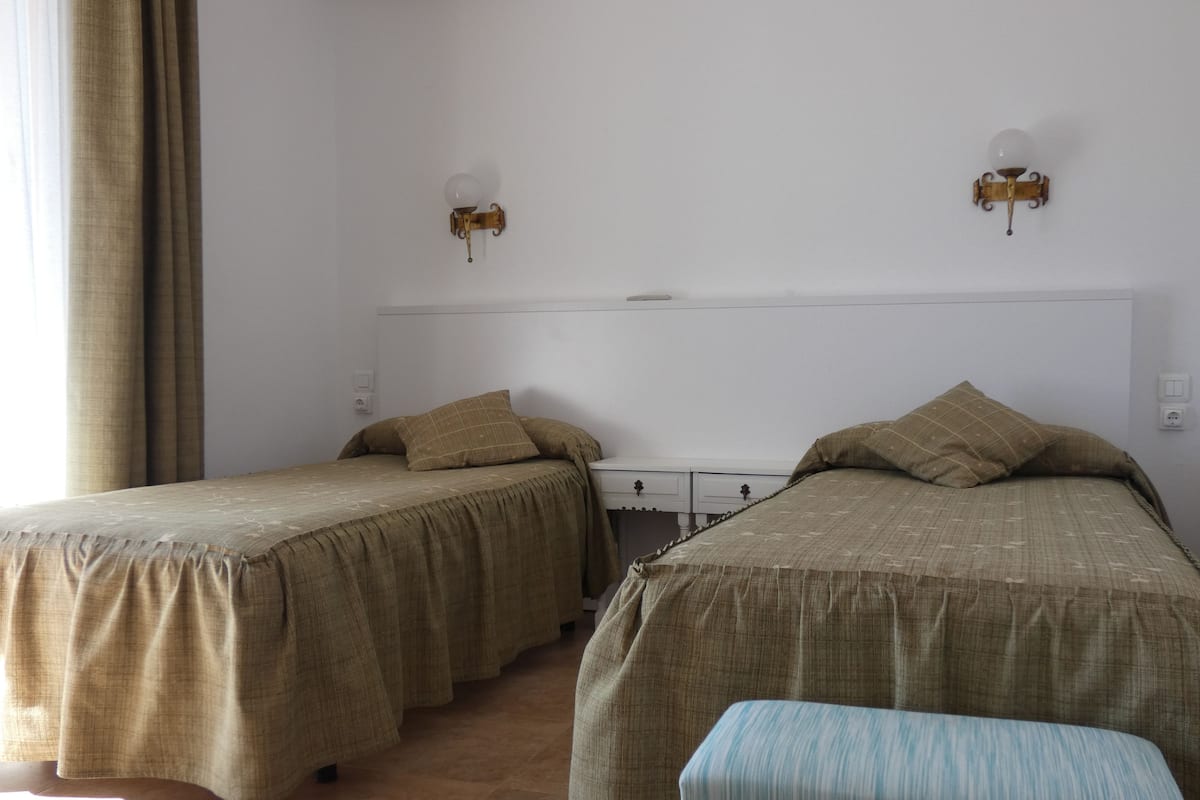 Een kamer met twee eenpersoonsbedden, een bankje en een bureau met een stoel.